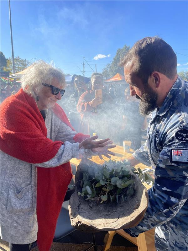 Woman in red scarf participates in smoking ceremony conducted by RAAF Officer
