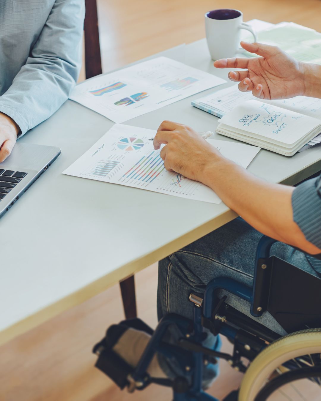 A person with disability sits at a desk working on goals and career aspirations with another person.