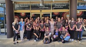 A group of women wearing indigenous patterned shirts stand in front of the gym where Her Futures Wellbeing Program takes place.